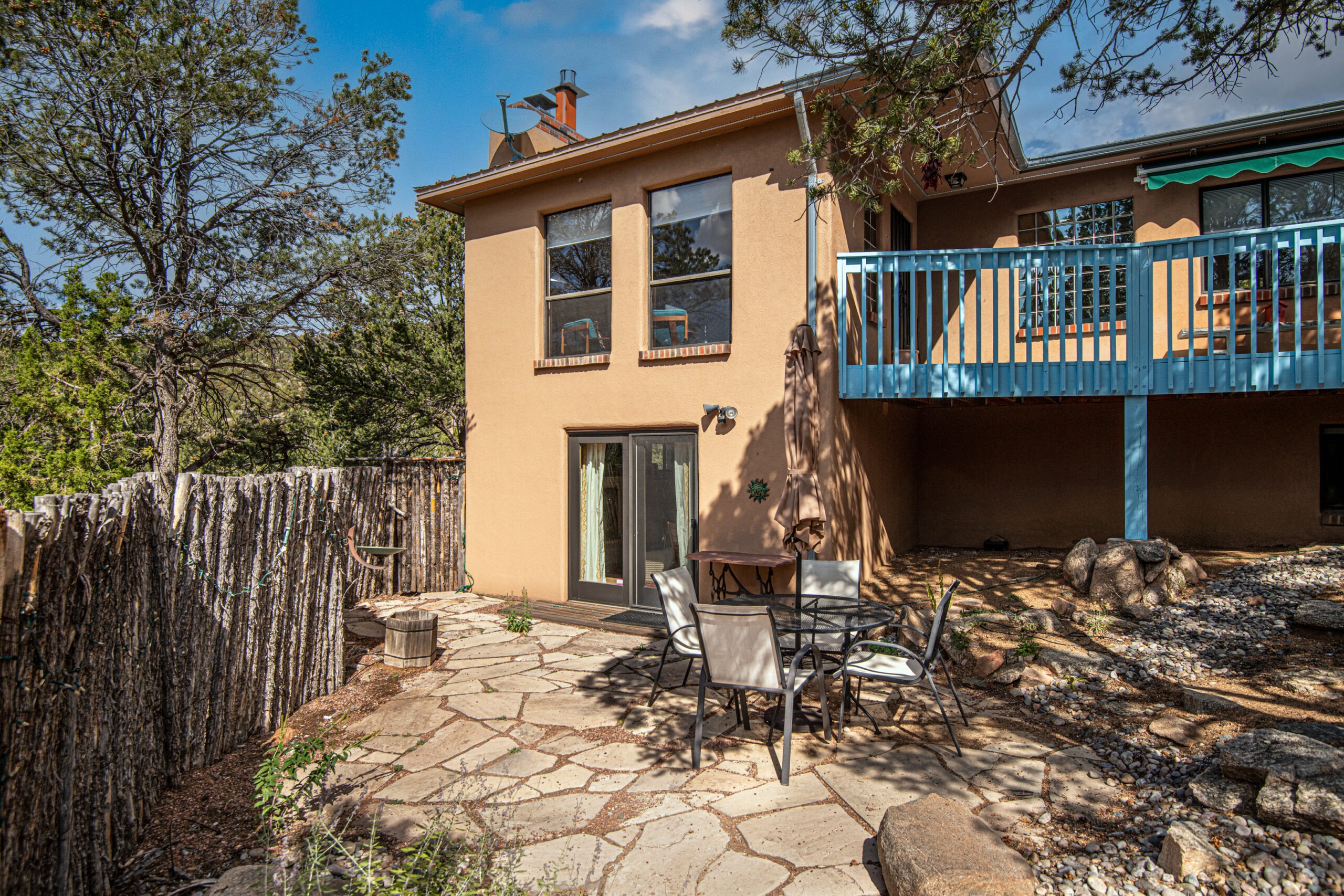 Patio of a two-story stucco home with stone flooring, a round table, umbrella, and chairs