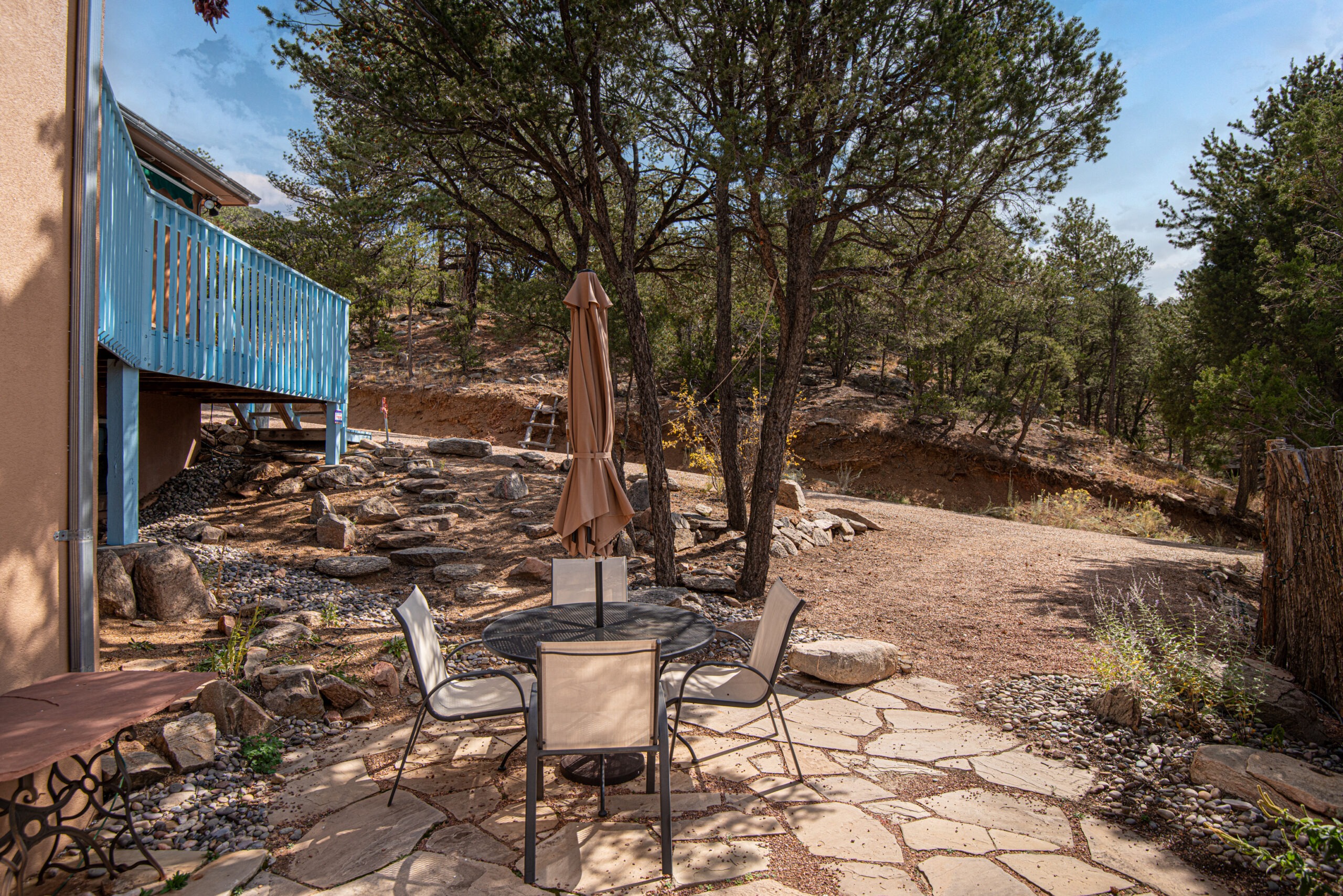 Patio with beige umbrella, surrounded by four chairs on stone tiles